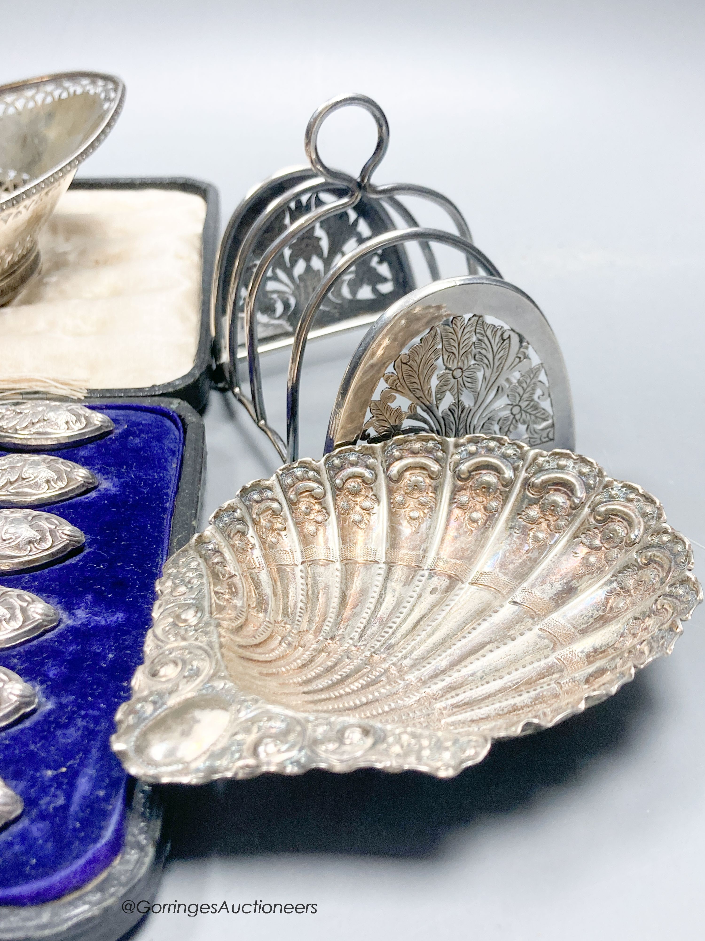 A George V silver two handled butter dish, with blue glass liner, a white metal basket, a pair of Victorian shell dishes, a French white metal dish, white metal toast rack and cased tea knives.